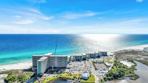 A coastal hotel with multiple buildings, a parking lot, and a beach.