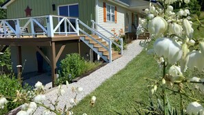 A two-story building with a deck, a staircase, and a garden with white flowers. - Cozy Family Getaway • Pet Friendly • Sleeps 8 • Near RRG • Campton, KY  (Campton)