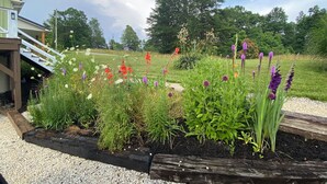 A garden with various flowers and a wooden deck. - Cozy Family Getaway • Pet Friendly • Sleeps 8 • Near RRG • Campton, KY  (Campton)