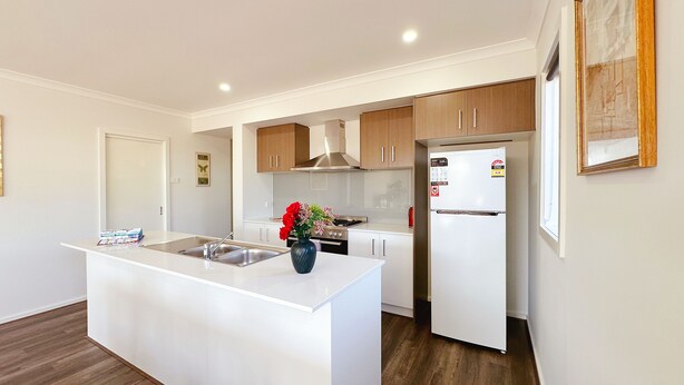 A modern kitchen with white cabinetry, a central island with a sink, a stove, and a refrigerator.