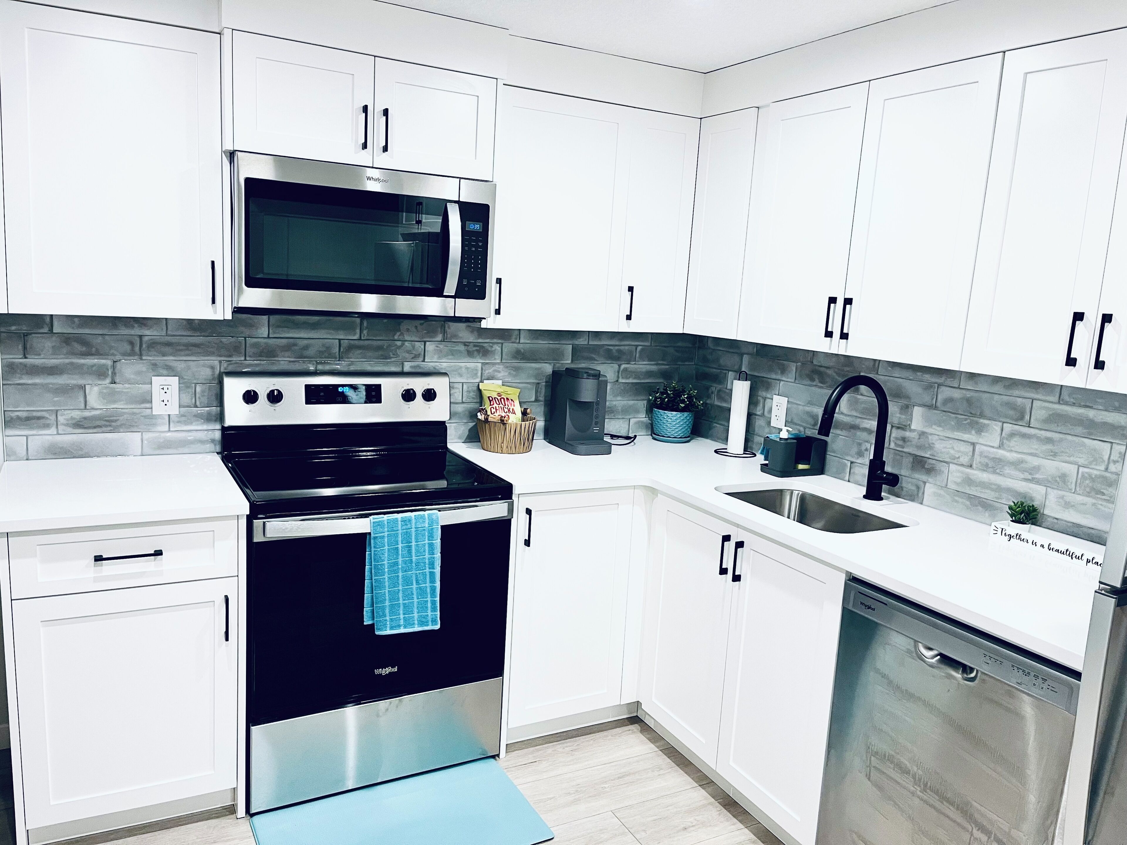 A modern kitchen with white cabinets, a stainless steel microwave, a black stove, and a sink with a black faucet.
