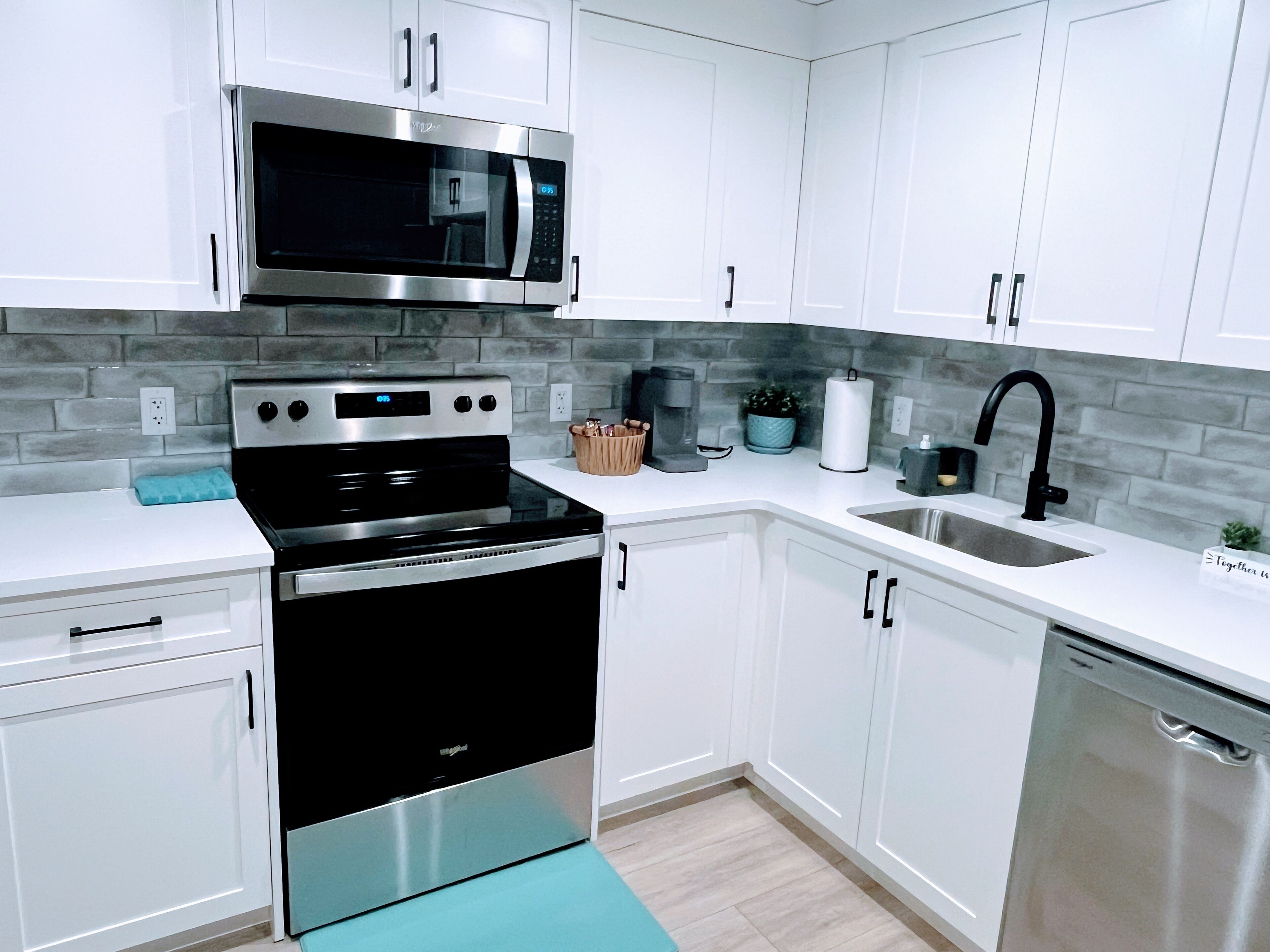 A modern kitchen with white cabinets, a stainless steel microwave, a black stove, and a sink with a black faucet.