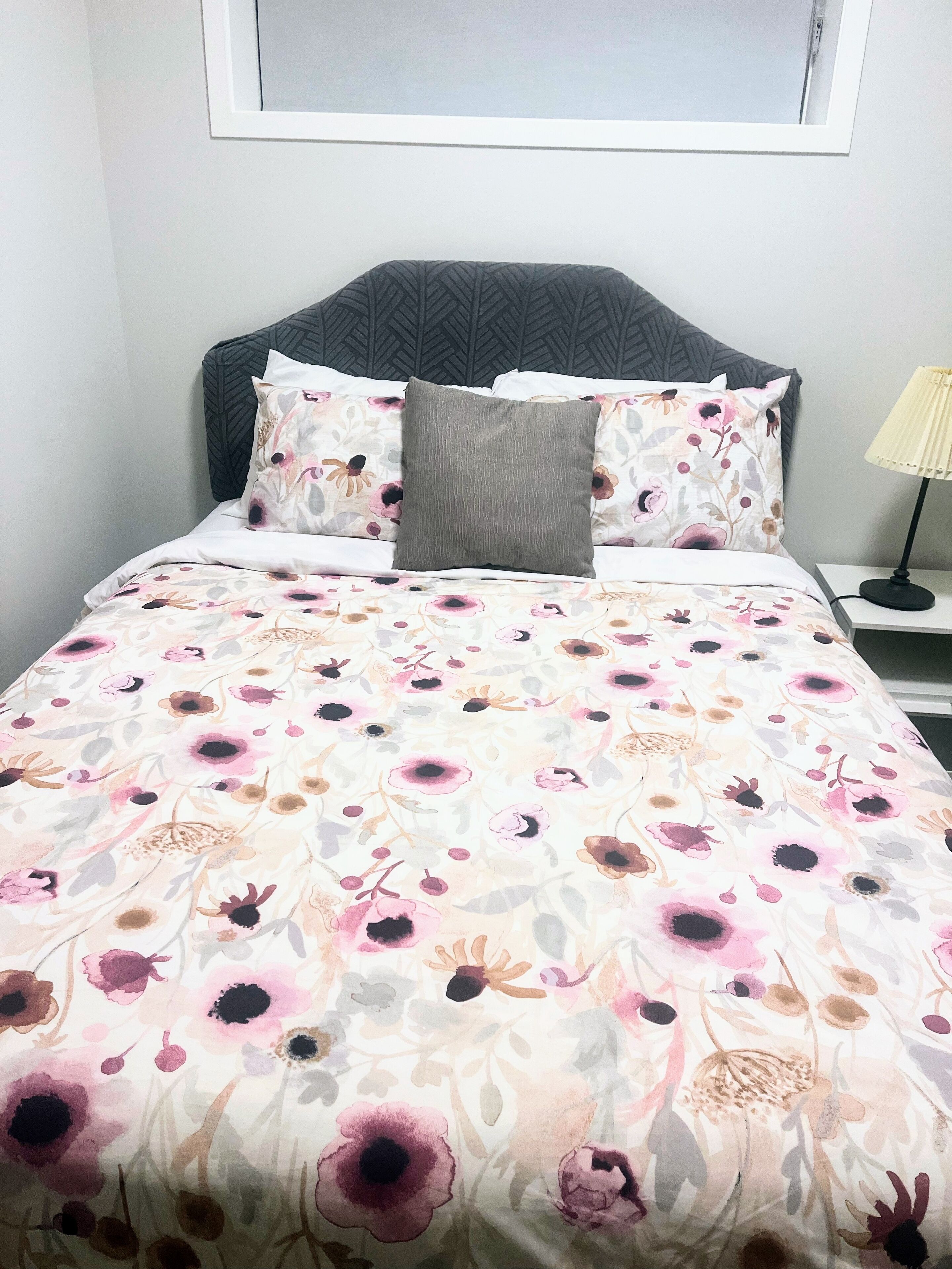 A bed with a floral bedspread, a grey pillow, and a headboard with a geometric pattern.