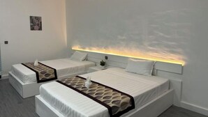 A hotel room with two single beds, a small bedside table, a wall-mounted air conditioner, and a painting on the wall. - The Aura Residence (Sihanoukville)