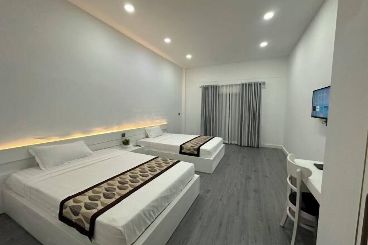 A modern hotel room with two beds, a desk, and a TV.