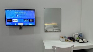 A hotel room with a flat-screen TV mounted on the wall displaying various streaming services, a white desk with a chair, a mirror, and a tray with cups and a kettle. - The Aura Residence (Sihanoukville)