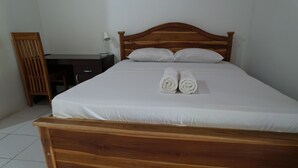 Una cama bien hecha con sábanas blancas y dos toallas enrolladas, un cabecero de madera y una mesita de noche con una lámpara.