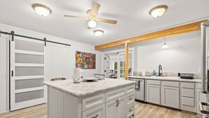 Une cuisine spacieuse dotée d’un grand îlot central, de meubles blancs et d’un ventilateur de plafond.