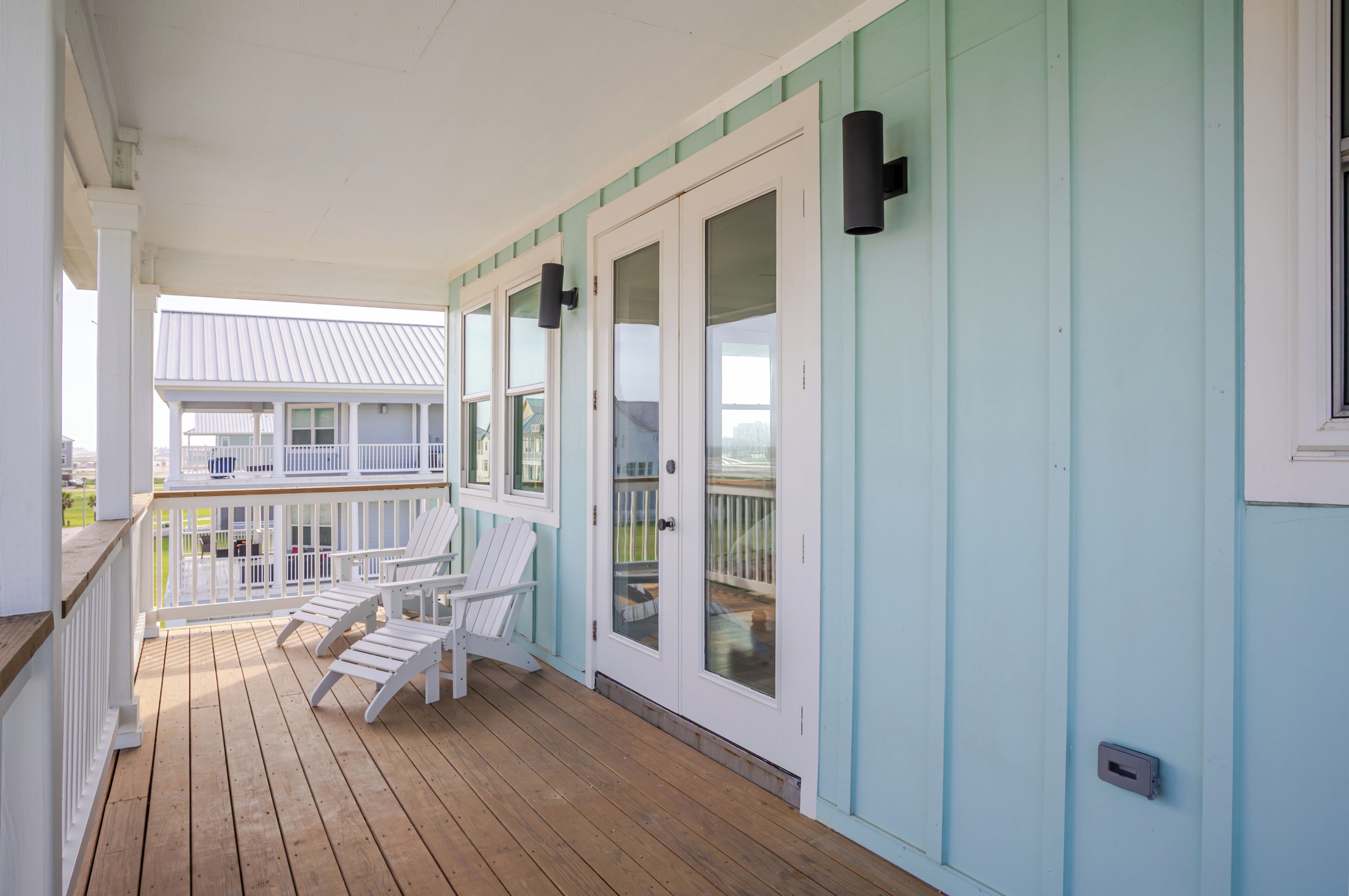 A covered porch with two white Adirondack chairs, a wooden deck, and a light blue exterior wall.