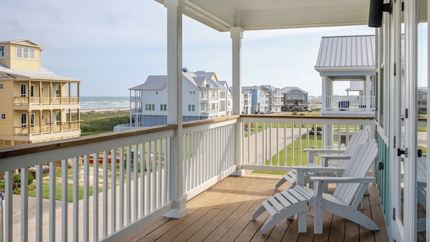 Une terrasse en bois avec des rampes blanches, donnant sur une plage et des immeubles résidentiels.