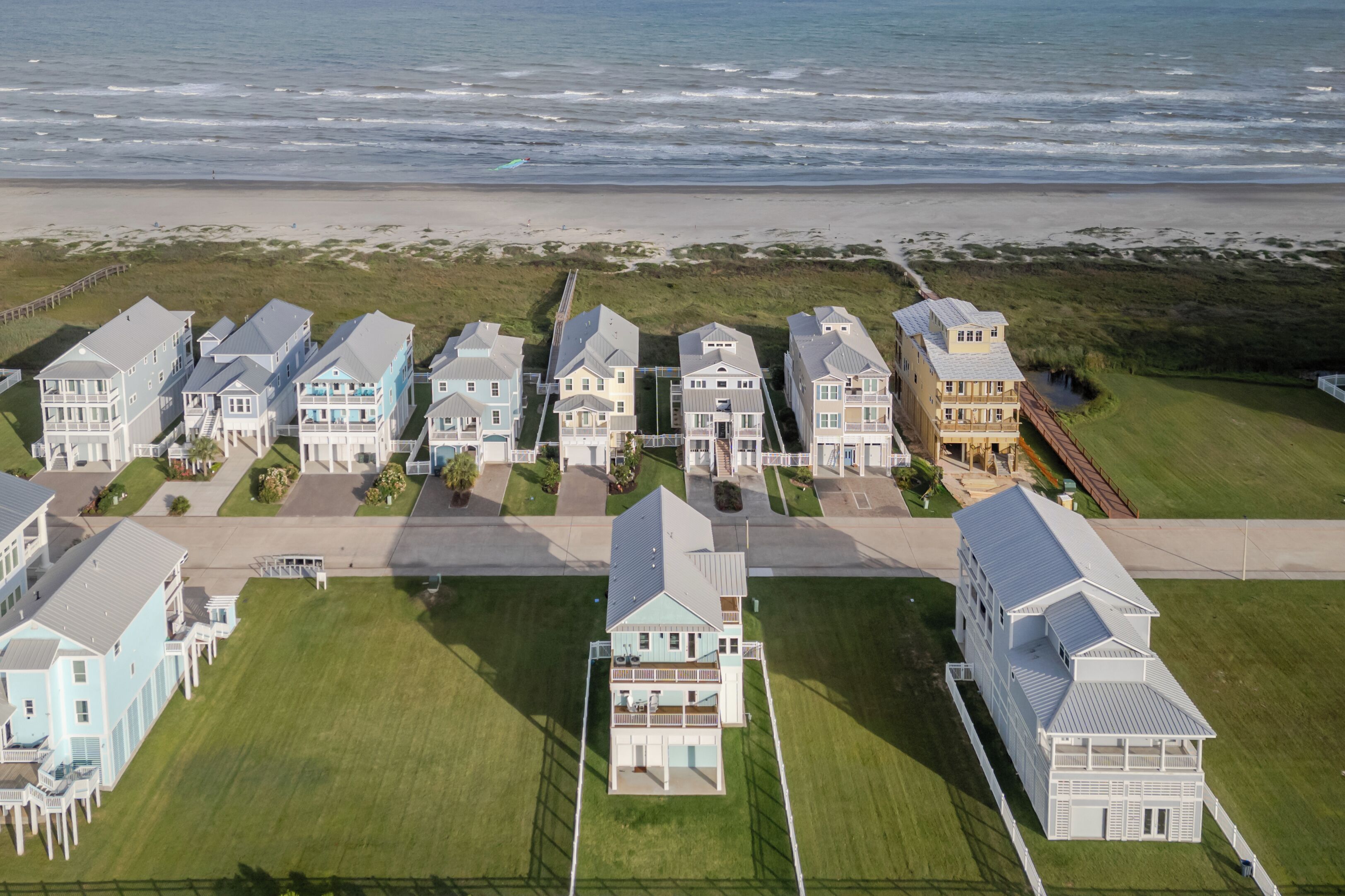 Een woongebied aan de kust met meerdere twee verdiepingen tellende huizen, een strand op de achtergrond en een verzorgd gazon.
