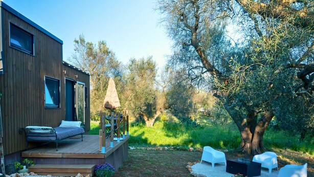 Ein modernes Haus mit einer Terrasse, Sitzgelegenheiten im Freien und einem Garten.