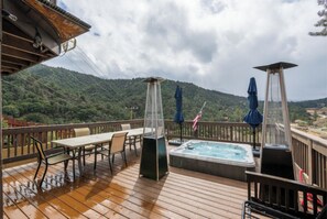 A wooden deck with a hot tub, outdoor furniture, and a view of a forested hill. - Scenic Frazier Park Cabin Stay (Frazier Park)