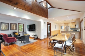 A spacious living room with a wooden ceiling, a large dining table, and a kitchen area with wooden cabinets and a refrigerator. - Lakefront, Kayaks Included, Come Unwind In Lenox! (Lenox)