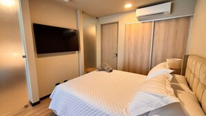 Un dormitorio con una cama, un televisor montado en la pared y un equipo de aire acondicionado sobre la cama.