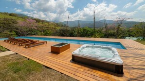 Una terraza de madera con un jacuzzi, sillas de descanso y una piscina con vistas a un paisaje montañoso.