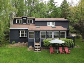 Ett tvåvåningshus med en täckt uteplats, en liten veranda och ett set röda Adirondack-stolar.