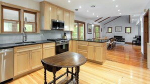 Une cuisine moderne avec des meubles en bois, un îlot central et un coin repas agrémenté d’un piano.