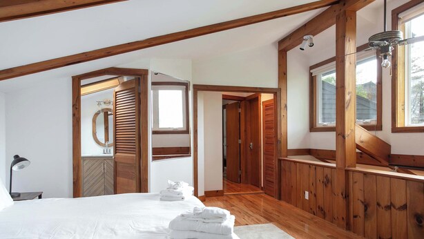 Une chambre avec un grand lit, des poutres en bois, une lucarne et une vue sur l’extérieur.