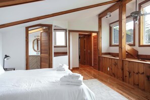 Un dormitorio con una cama grande, vigas de madera, tragaluces y vistas al exterior.