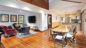 Un vaste espace de vie doté d’un plancher en bois, d’une grande table à manger et d’un téléviseur fixé au mur.