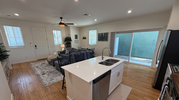 A modern kitchen with a central island, a dining area with a sofa and chairs, and a large sliding glass door leading to a balcony. - Lux Midtown; Mins to Uptown, Biltmore, Melrose District, Papago Park, & Sports (Phoenix)