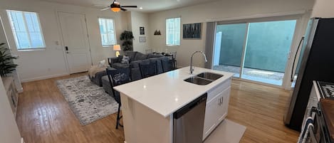 A modern kitchen with a central island, a dining area with a sofa and chairs, and a large sliding glass door leading to a balcony.
