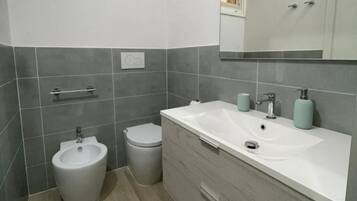 Ein Badezimmer mit einer Bidet-Funktion, Toilette und einem Waschtisch mit Waschbecken und Spiegel.