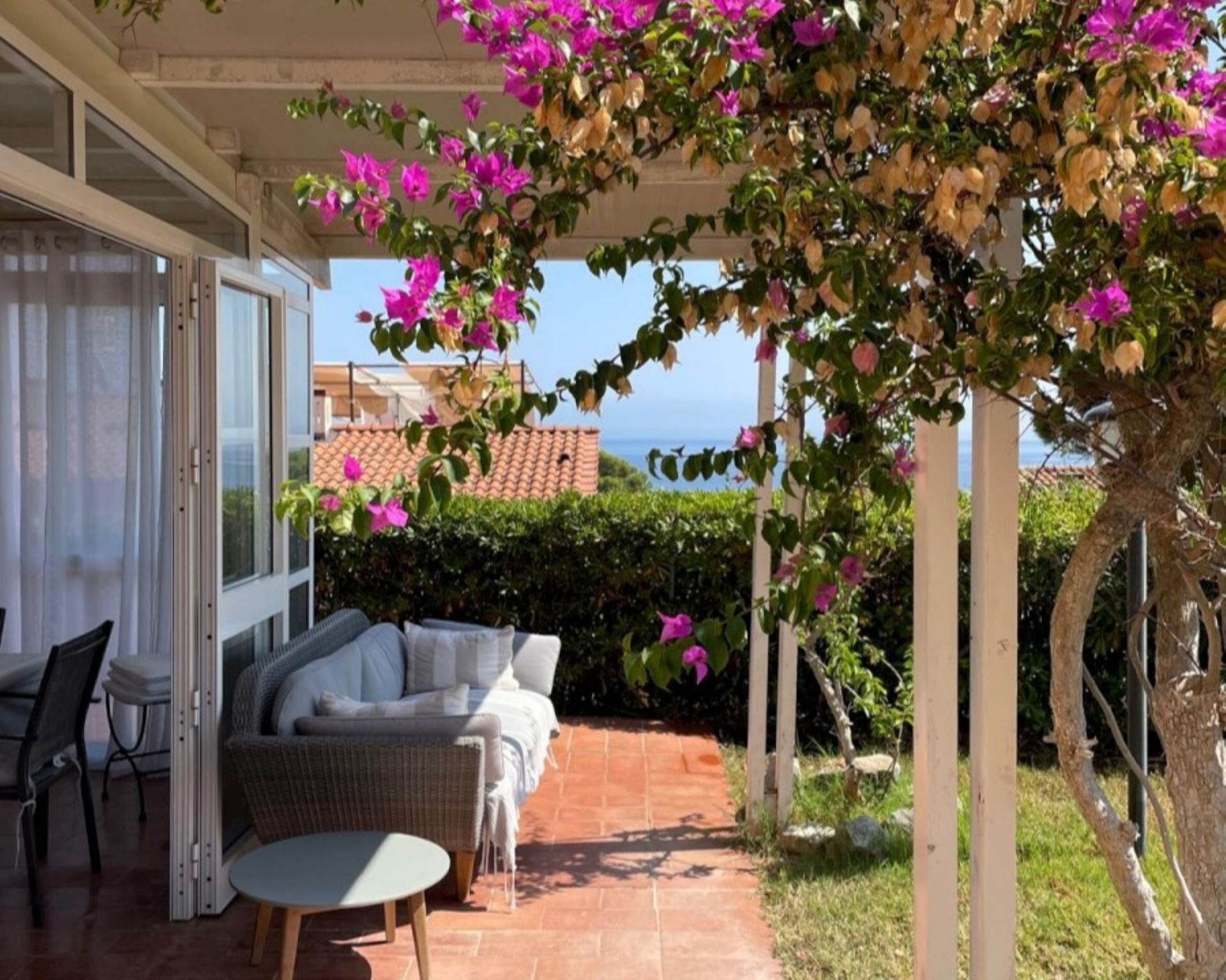 Une terrasse extérieure dotée d’une pergola blanche, d’un canapé en osier et d’une table.