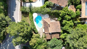 An aerial view of a residential area with a swimming pool surrounded by lush greenery and a tiled-roofed house.