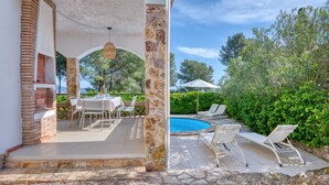 A covered outdoor area with a pool, lounge chairs, and a table set for dining.