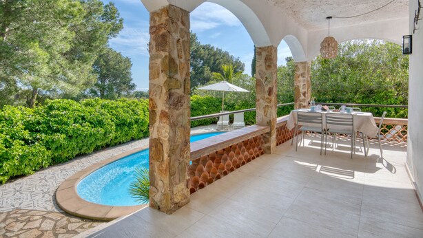 A covered outdoor area with a pool, stone pillars, and a table with chairs.
