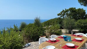 A table set for dining with a view of the sea, surrounded by greenery and white chairs. - Villetta Fonza, with a wonderful sea view! (Campo nell'Elba)