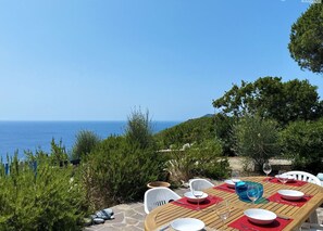 Mesa lista para comer con vista al mar, rodeada de follaje y sillas blancas.