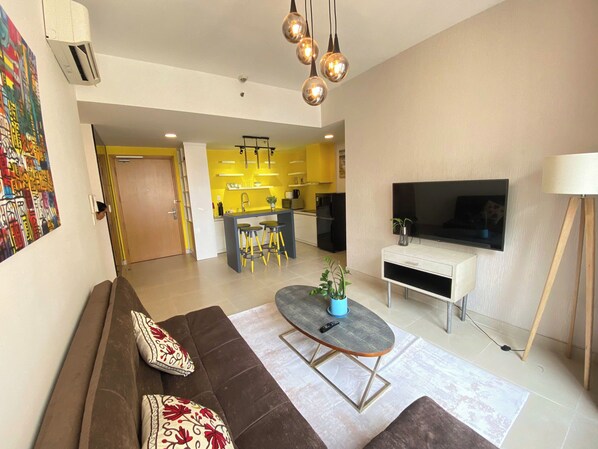 A modern living room with a sofa, a coffee table, a TV, and a kitchen in the background. - MASTERI THAO DIEN PREMIER APARTMENTS (Ho Chi Minh City)