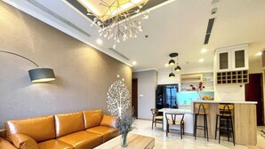 Una sala moderna con un sofá de cuero marrón, una mesa de centro de madera y una escultura decorativa de un árbol. Hay una zona de cocina con una barra y taburetes.