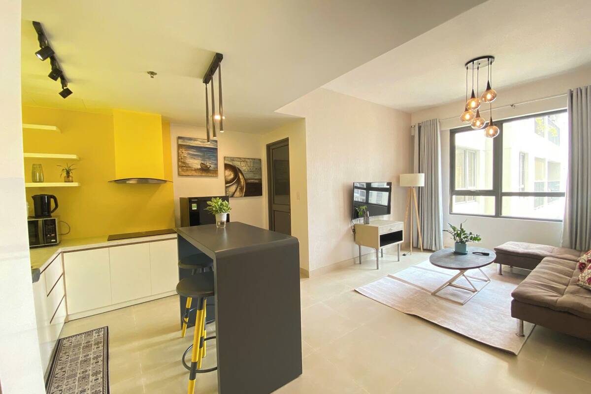 Een modern appartement met keuken, eethoek en woonkamer. Het heeft een groot raam, een bank en een televisie.