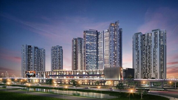 Un moderno complejo de edificios de gran altura con múltiples torres residenciales, un puente peatonal y una zona ribereña bien iluminada.