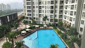 Una piscina rectangular rodeada de palmeras y sillas de descanso, con un rascacielos al fondo.