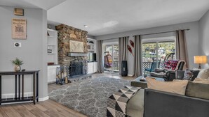 Un vaste salon agrémenté d’une cheminée en pierre, d’une grande fenêtre offrant une vue sur les environs, et d’un coin salon confortable avec un canapé et des fauteuils.