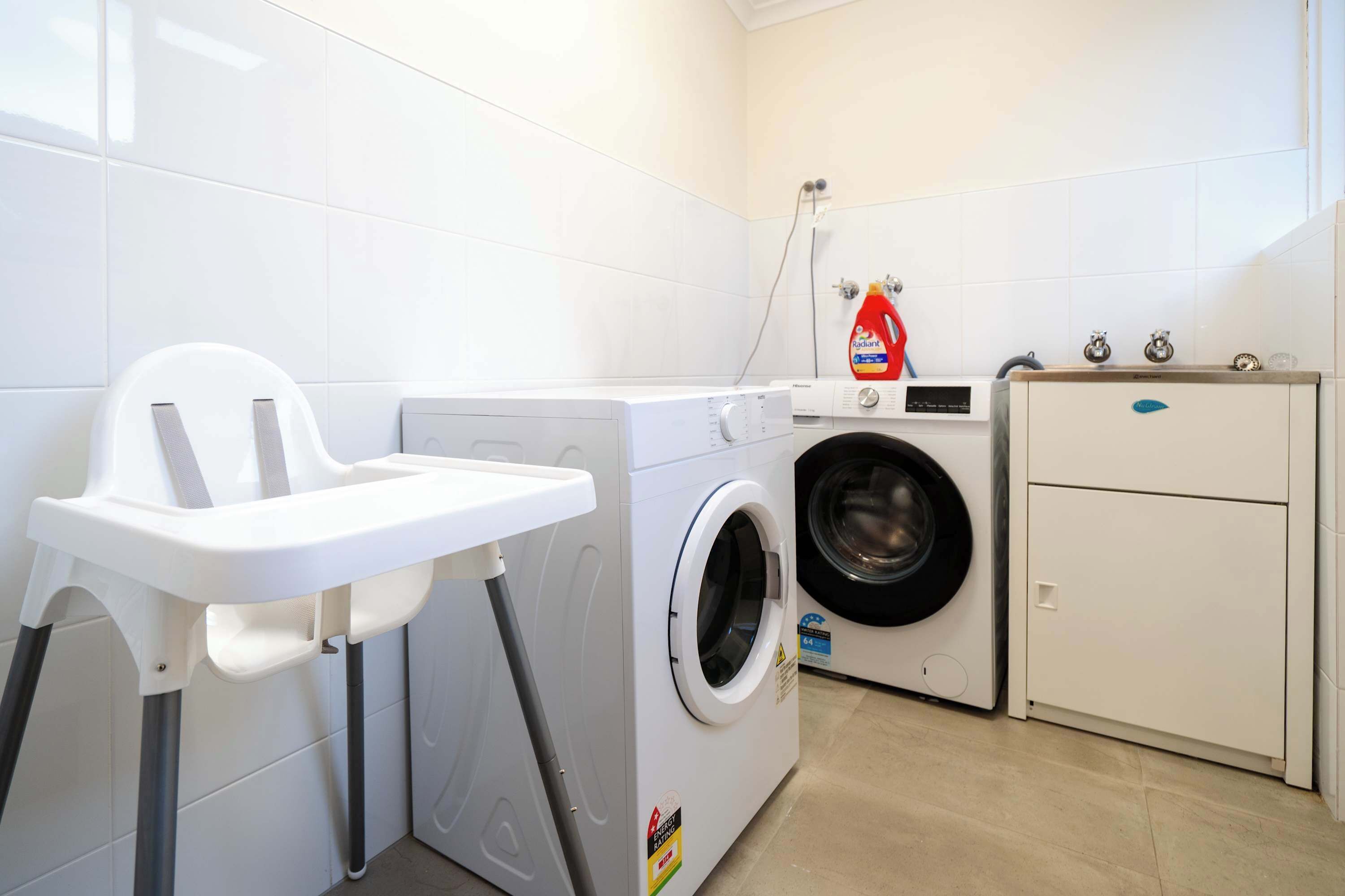 Un área de lavandería con lavadora, secadora, un armario y una silla blanca.