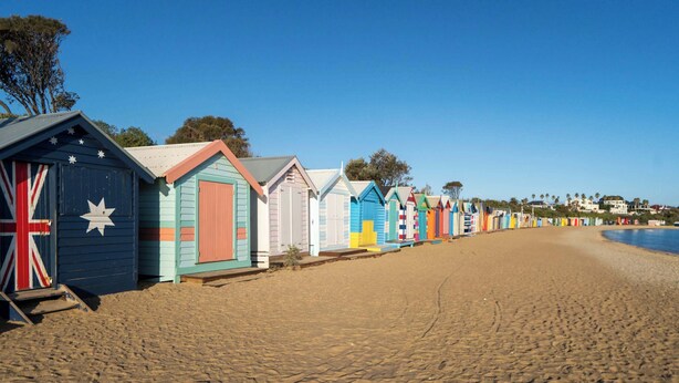 Une rangée de cabanes de plage colorées le long d’une plage de sable.
