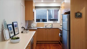 Une cuisine compacte avec des meubles en bois, un réfrigérateur en acier inoxydable et une fenêtre donnant sur l’extérieur.