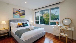 Une chambre à coucher comprenant un lit, des lampes de chevet, une commode, un miroir et une fenêtre donnant sur un paysage verdoyant.