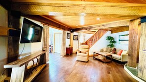 Un vaste espace de vie doté d’un plafond en bois, d’un téléviseur à écran plat fixé au mur, d’un canapé, d’une table basse et d’un escalier menant à un autre niveau.