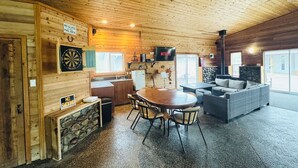 L’intérieur chaleureux d’un chalet avec un plafond en bois, un coin repas comprenant une table et des chaises, un canapé, une cheminée et un téléviseur.