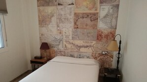 Ein Schlafzimmer mit einem Bett, einem Nachttisch, einer Lampe und einer mit Karten tapezierten Wand.
