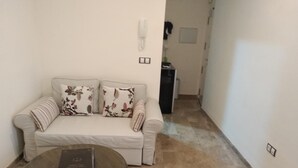 Ein Wohnzimmer mit einem beigefarbenen Sofa, floralen Kissen, einem gestreiften Kissen und einem runden Tisch mit einem Buch.