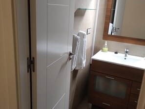 Een badkamer met een wit wastafelmeubel, een spiegel en een handdoek aan de deur.
