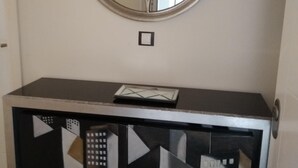 Ein Zimmer mit einem runden Spiegel an der Wand, einem kleinen Tisch mit einem untergebauten Schrank mit geometrischem Muster und einem Lichtschalter an der Wand.